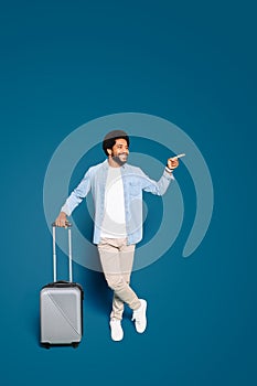 The jovial man standing with a suitcase, pointing aside, his face alight with enthusiasm