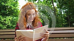 Jovial red haired girl laughing at funny book in park