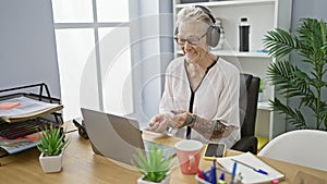 Jovial senior grey-haired business woman tapping into the rhythm at work, gleefully drumming her desk, enjoying music in office