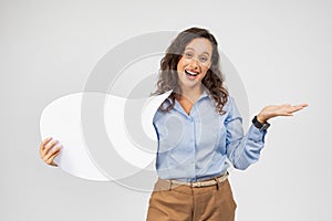 A jovial woman with curly hair and a blue shirt holds a blank white speech bubble sign