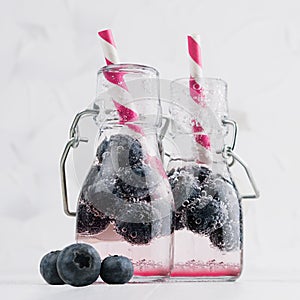 Joy bright fresh summer drinks with blueberry, straw, soda water in elegant yoke bottles on soft light white wood table, square.