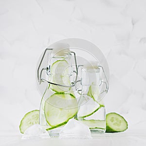 Joy bright fresh summer drinks with green cucumber, ice cubes, soda water in two elegant yoke bottles on soft light white wood.