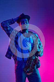 Joy of music. Modern musician, holds wind instrument, saxophone against gradient purple-pink background in neon light.