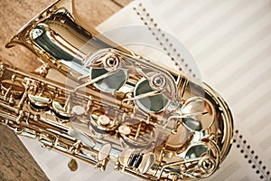 The joy of sax. Top view of beautiful shiny saxophone lying on sheets for music notes over wooden floor. Musical