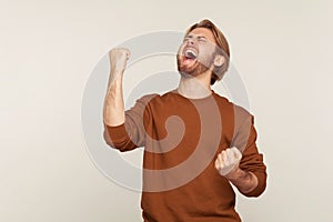 Joy of success, triumphal victory. Portrait of enthusiastic happy delighted man with beard in sweatshirt