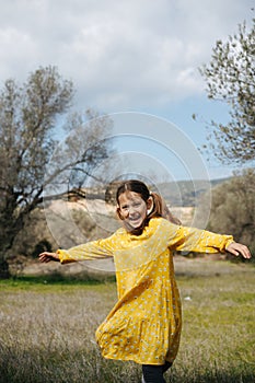 A joyful 8-year-old girl in a yellow dress is spinning in a field