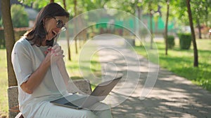 Joyful adorable beautiful business Senior woman wearing eyeglasses sittingin park outdoors, working on a laptop. Modern