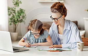 Joyful adult woman helping small girl to do homework in light spacious living room