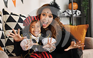 Joyful african american family mother and little boy son in Halloween costumes making scary gesture