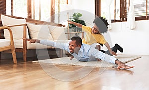 Joyful African American Father and little son playing aeroplane on floor together at home. Happy Smiling kid boy flying on Dad