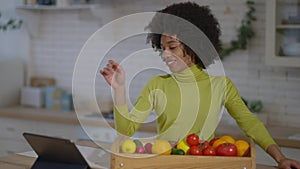 Joyful African American housewife searching online recipe on tablet standing in kitchen with raw vegetables. Portrait of