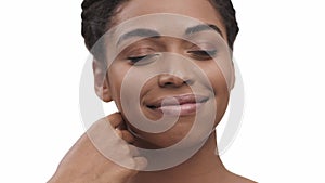 Joyful african american lady touching her smooth skin, enjoying perfect face condition, white studio background, close