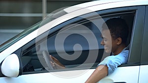 Joyful African-American teen boy sitting on driver place, first car purchase