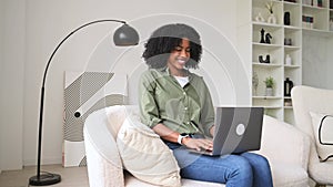 A joyful African-American woman comfortably works on her laptop at home