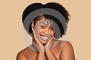 Joyful african american woman with hands on cheeks and curly hair, beige backdrop