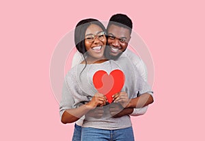 Joyful african couple holding big red heart together