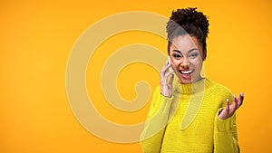 Joyful african female talking phone on yellow background, mobile communication