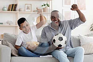 Joyful african grandfather and hid grandson cheering while watching football on tv