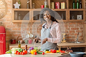 Joyful african lady mixing veggies in bowl in kitchen