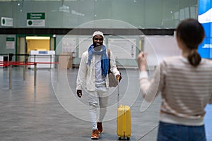 Happy african man employee with luggage going to female waiting for him with sign board in airport