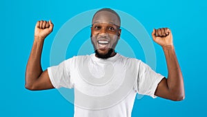 Joyful African Man Shaking Fists Looking At Camera, Blue Background