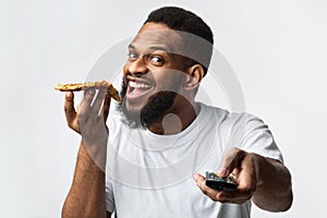 Joyful African Millennial Man Eating Pizza Watching TV In Studio