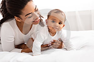 Joyful African Mommy Playing With Toddler Baby On Bed Indoor