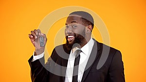 Joyful afro-american man in suit showing automobile keys, renting car, leasing