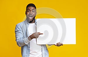 Joyful afro guy holding and pointing at white advertising board