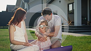 Joyful american dream family are sitting outdoors on the lawn near the house on a purple blanket, carpet or rug. Parents