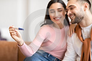 Joyful Arab Couple Hugging Celebrating Positive Pregnancy Test Sitting Indoor