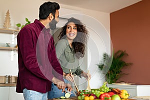 Joyful arab spouses cooking dinner and chatting, preparing fresh salad together in kitchen interior, free space