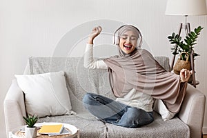 Joyful arabic girl in wireless headphones listening music at home