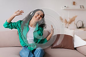 Joyful Arabic Woman Listening To Music Online Wearing Earphones Indoors