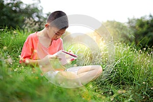 Joyful asian boy student sitting writing and reading book outside on school or park.