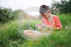 Joyful asian boy student sitting writing and reading book outside on school or park.