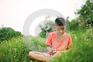 Joyful asian boy student sitting writing and reading book outside on school or park.