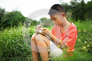 Joyful asian boy student sitting writing and reading book outside on school or park.