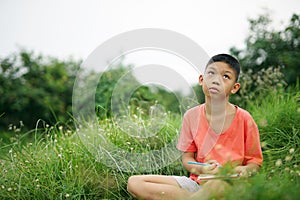 Joyful asian boy student sitting writing and reading book outside on school or park.