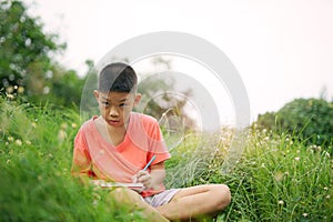 Joyful asian boy student sitting writing and reading book outside on school or park.