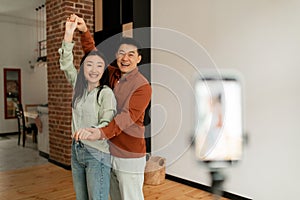 Joyful asian couple broadcasting while dancing and having fun at home, vloggers recording video in front of smartphone