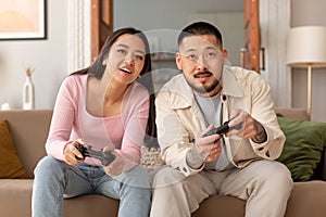 Joyful Asian Couple Playing Video Game Holding Joysticks At Home