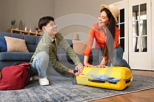 Joyful Asian Tourists Couple Packing Travel Suitcase At Home