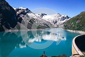 Joyful attitude of a young man climbing a rock from which he sees the entire Stausee Mooserboden with adjacent Kaprun glacier in