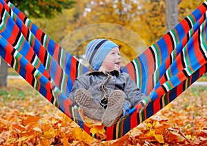 Joyful baby boy in autumn park on a hammock