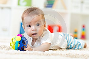 Joyful baby lying on the carpet in nursery room