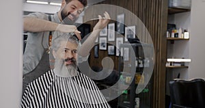 Joyful barber cutting hair and talking to client loking at mirror in barbershop