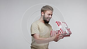 Joyful bearded man slowly opening gift box, unwrapping birthday surprise and expressing great happiness amazement