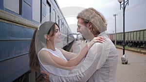 Joyful beautiful girl hugs boyfriend and laughs near train wagon on railway platform after separation