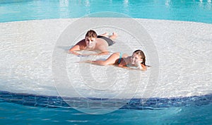 Joyful beautiful smiling little girl and teenage boy relaxing in swimming pool island on summer beautiful gorgeous day